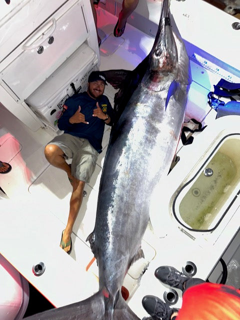 A man proudly holds a large blue marlin, showcasing the impressive size and vibrant color of the fish.