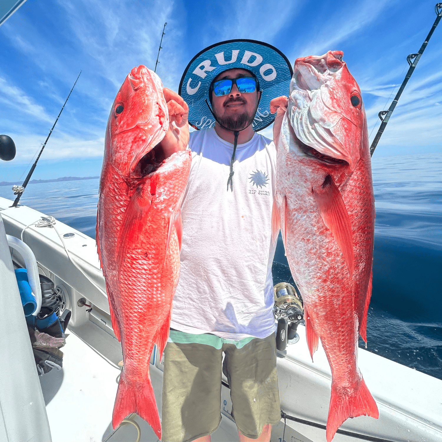 A man on a boat proudly holds two vibrant red fish, showcasing his successful catch.