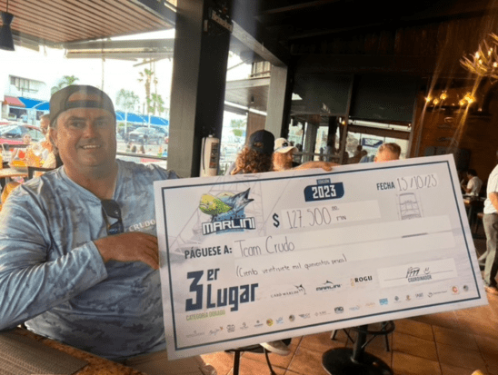 A man proudly displays a large check while standing in a restaurant, showcasing a moment of celebration.